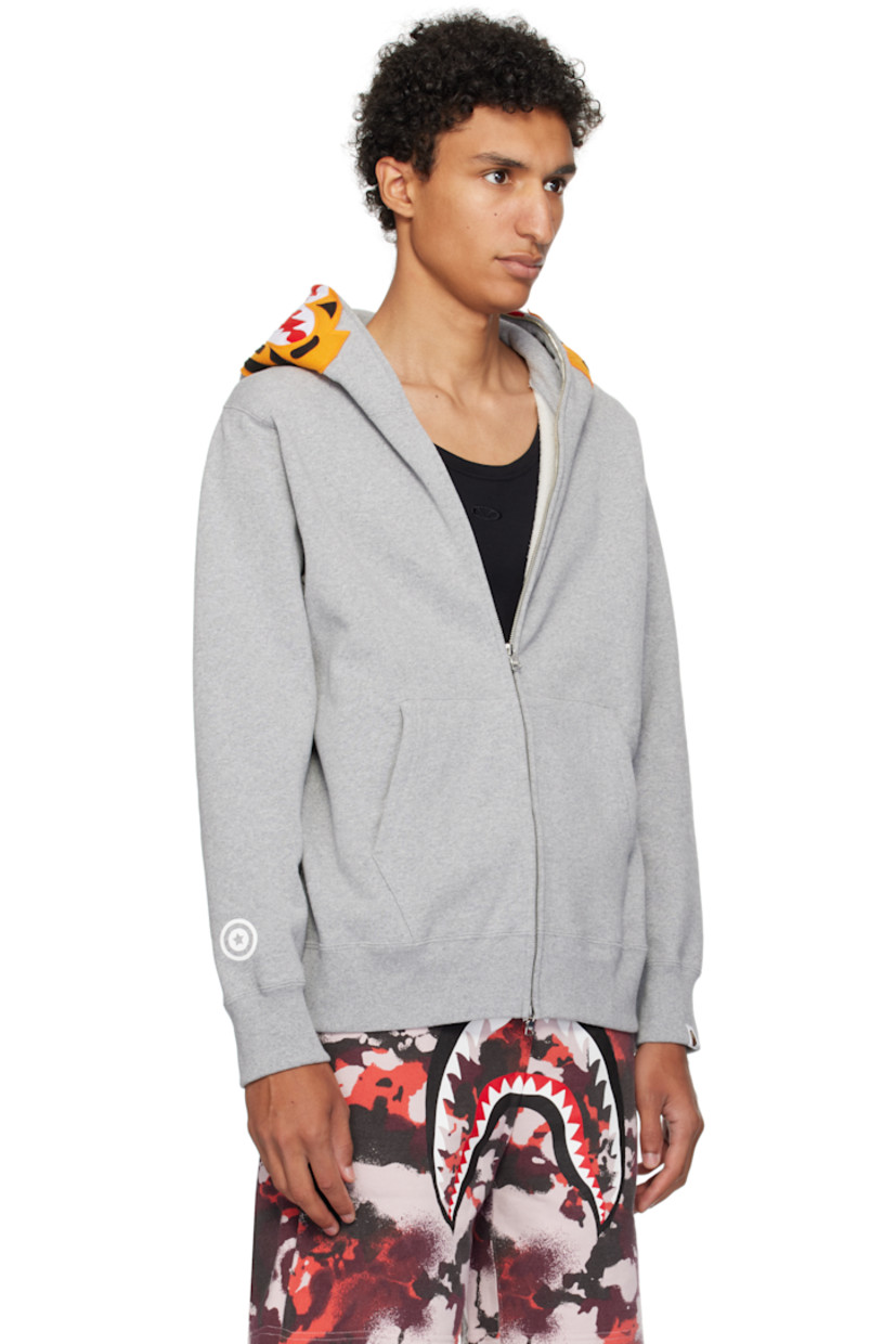 Cotton fleece hoodie. 

· Graphic patches and embroidered text at hood
· Graphics printed at hood and sleeves
· Two-way zip closure extends to hood
· Patch pockets
· Rib-knit hem and cuffs
· Dropped shoulders
· Logo flag at cuff

Supplier color: Gray
