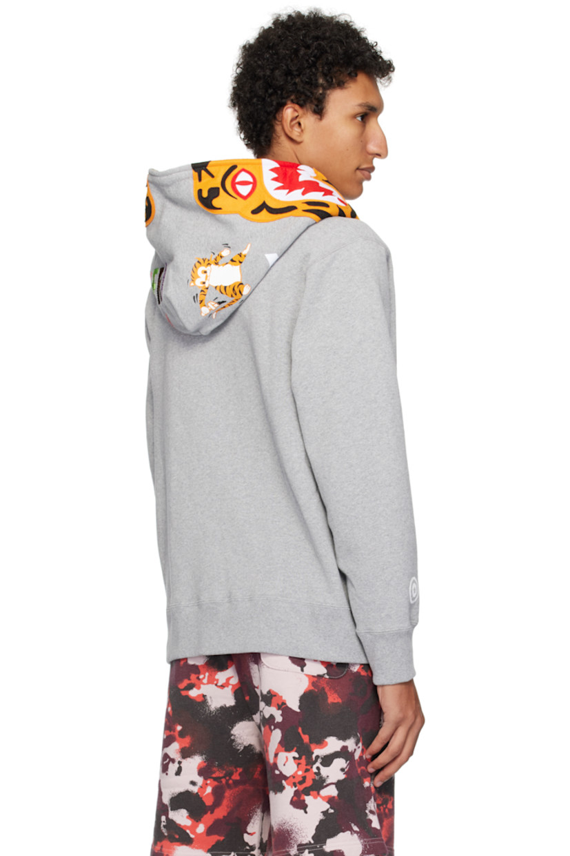 Cotton fleece hoodie. 

· Graphic patches and embroidered text at hood
· Graphics printed at hood and sleeves
· Two-way zip closure extends to hood
· Patch pockets
· Rib-knit hem and cuffs
· Dropped shoulders
· Logo flag at cuff

Supplier color: Gray
