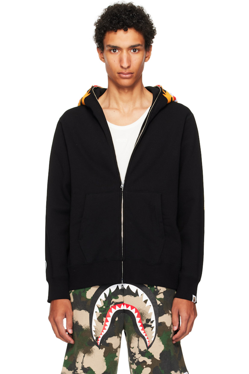 Cotton fleece hoodie. 

· Graphic patches and embroidered text at hood
· Graphics printed at hood and sleeves
· Two-way zip closure extends to hood
· Patch pockets
· Rib-knit hem and cuffs
· Dropped shoulders
· Logo flag at cuff

Supplier color: Black