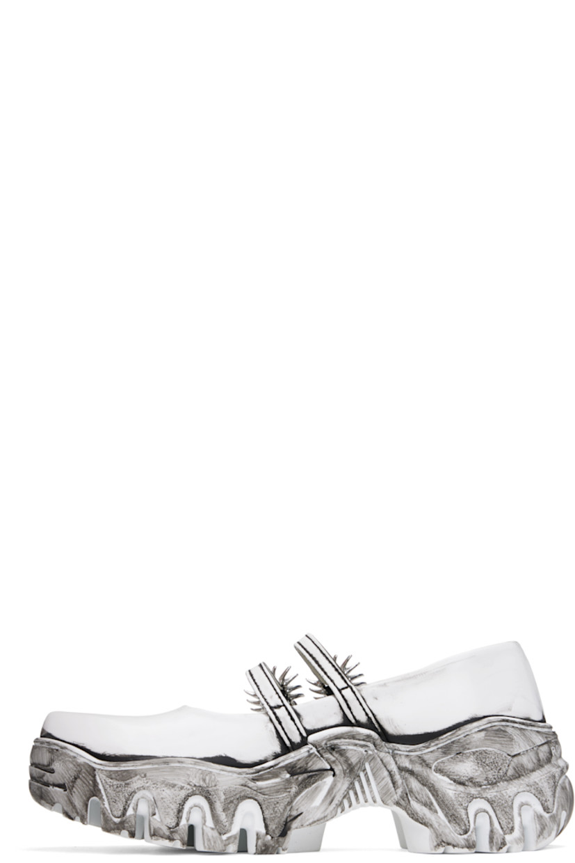 Buffed faux-leather Mary Jane-style loafers in white.

· Bureau Veritas-certified faux-leather
· Smudging throughout
· Partially elasticized pin-buckle straps
· Logo hardware at outer side
· Logo embossed at heel
· Grained faux-leather lining
· Sculptural platform rubber midsole
· Treaded rubber sole
· Silver-tone graphic hardware
· Platform: H1.5"

Supplier color: Quantum