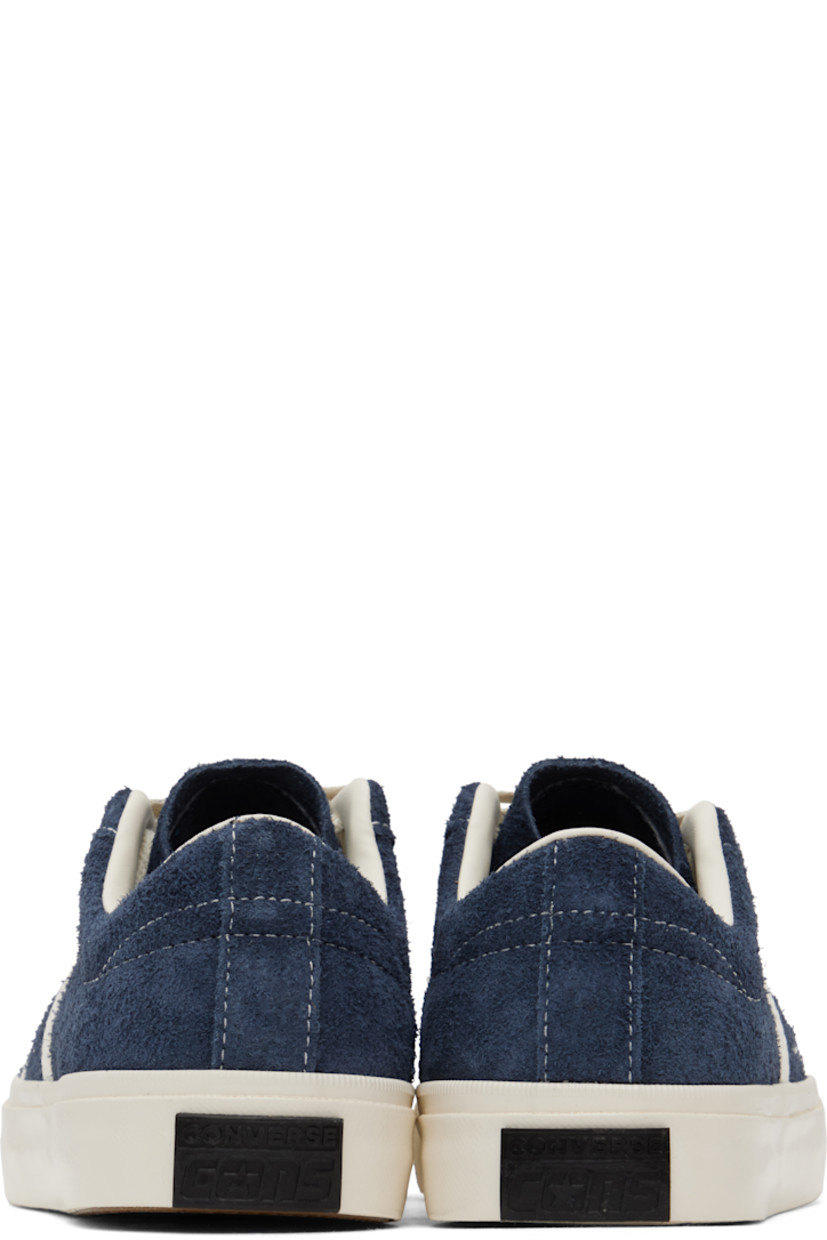 Low-top suede sneakers in navy.

· Lace-up closure
· Logo embossed at tongue
· Concealed elasticized gussets at tongue
· Padded collar
· Logo cutout at sides
· Perforations and canvas trim
· Rubberized logo patch at heel
· Cushioned CX foam footbed
· Buffed leather and canvas lining
· Treaded rubber sole

Supplier color: Navy/Egret/Egret