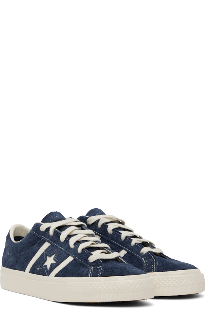 Low-top suede sneakers in navy.

· Lace-up closure
· Logo embossed at tongue
· Concealed elasticized gussets at tongue
· Padded collar
· Logo cutout at sides
· Perforations and canvas trim
· Rubberized logo patch at heel
· Cushioned CX foam footbed
· Buffed leather and canvas lining
· Treaded rubber sole

Supplier color: Navy/Egret/Egret