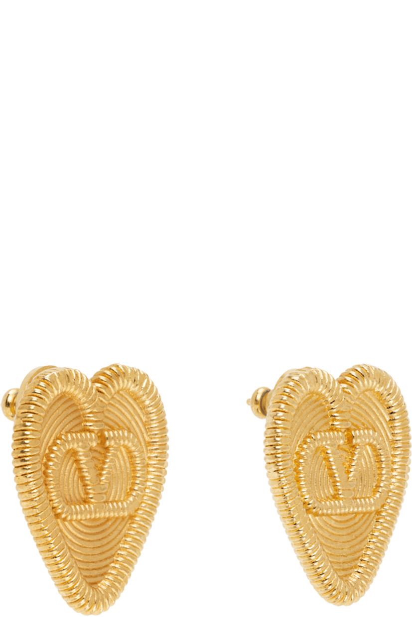 Pair of heart-shaped stud earrings in gold tone.

· Hammered detailing throughout
· Logo at face
· Post-stud fastening 
· H1" x W1"

Supplier color: Antique brass
