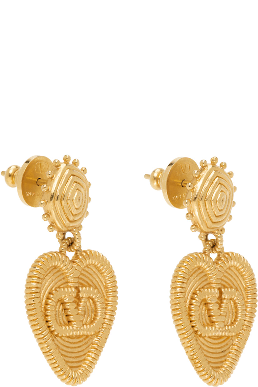 Pair of heart-shaped drop earrings in gold tone.

· Hammered detailing throughout
· Logo at drop
· Post-stud fastening
· H1.25" x W0.75"

Supplier color: Antique brass