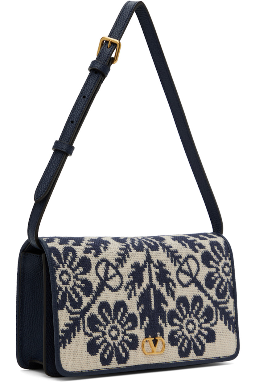 Canvas and grained leather shoulder bag in beige and navy.

· Jacquard floral pattern throughout
· Adjustable and detachable shoulder strap
· Logo hardware at face
· Magnetic flap closure
· Zip pocket at interior 
· Three card slots
· Buffed nappa leather lining 
· Gold-tone hardware
· H5" x W8" x D2"

Supplier color: Avorio blue/Dark