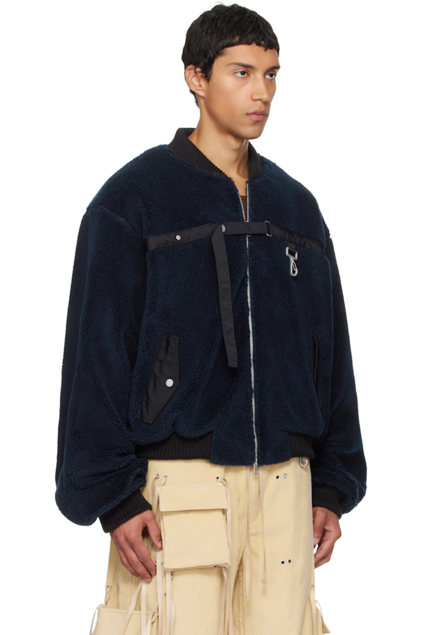 Sherpa fleece bomber jacket.

· Heavyweight 
· Rib-knit stand collar, hem, and cuffs
· Cinch strap and logo-engraved clasp at chest
· Flap pockets at front
· Logo patch at cuff
· Full mesh lining

Supplier color: Navy/Black