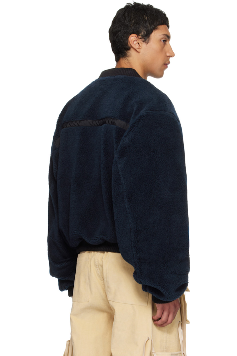 Sherpa fleece bomber jacket.

· Heavyweight 
· Rib-knit stand collar, hem, and cuffs
· Cinch strap and logo-engraved clasp at chest
· Flap pockets at front
· Logo patch at cuff
· Full mesh lining

Supplier color: Navy/Black