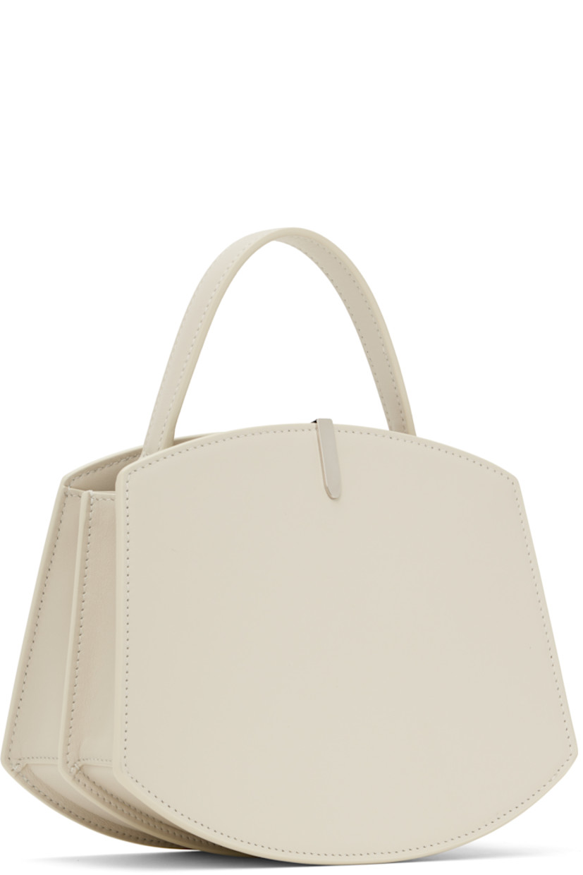 Structured buffed calfskin top handle bag in off-white.

· Carry handle at top
· Silver-tone hardware at face
· Accordion panel at sides
· Silver-tone logo stamp at back face
· Magnetic tab closure 
· Card slot at two compartment interior
· Buffed calfskin lining
· H6.75" x W8.25" x D4"

Supplier color: Ivory