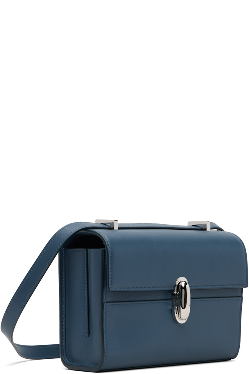 Rigid buffed calfskin shoulder bag.

· Adjustable crossbody strap
· Shorten to shoulder strap with interior studs
· Foldover flap with turn-lock clasp
· Two-compartment leather interior
· Two patch pockets
· H5.5" x W7.5" x D2.75"

Supplier color: Ocean