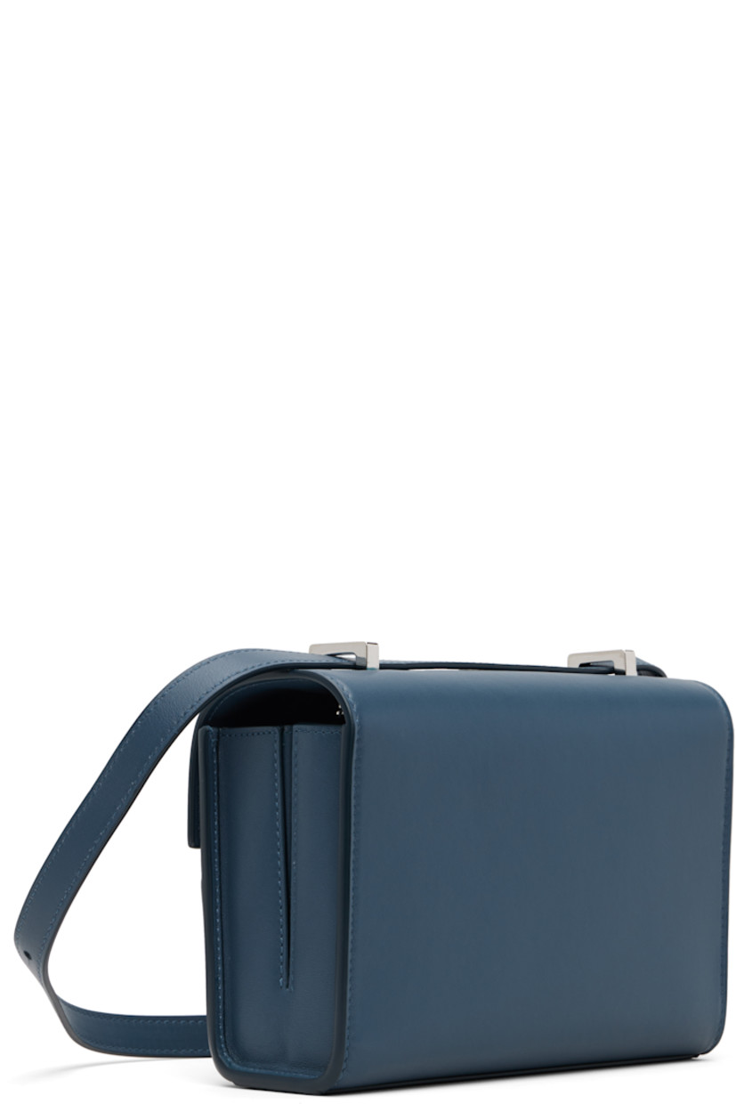 Rigid buffed calfskin shoulder bag.

· Adjustable crossbody strap
· Shorten to shoulder strap with interior studs
· Foldover flap with turn-lock clasp
· Two-compartment leather interior
· Two patch pockets
· H5.5" x W7.5" x D2.75"

Supplier color: Ocean