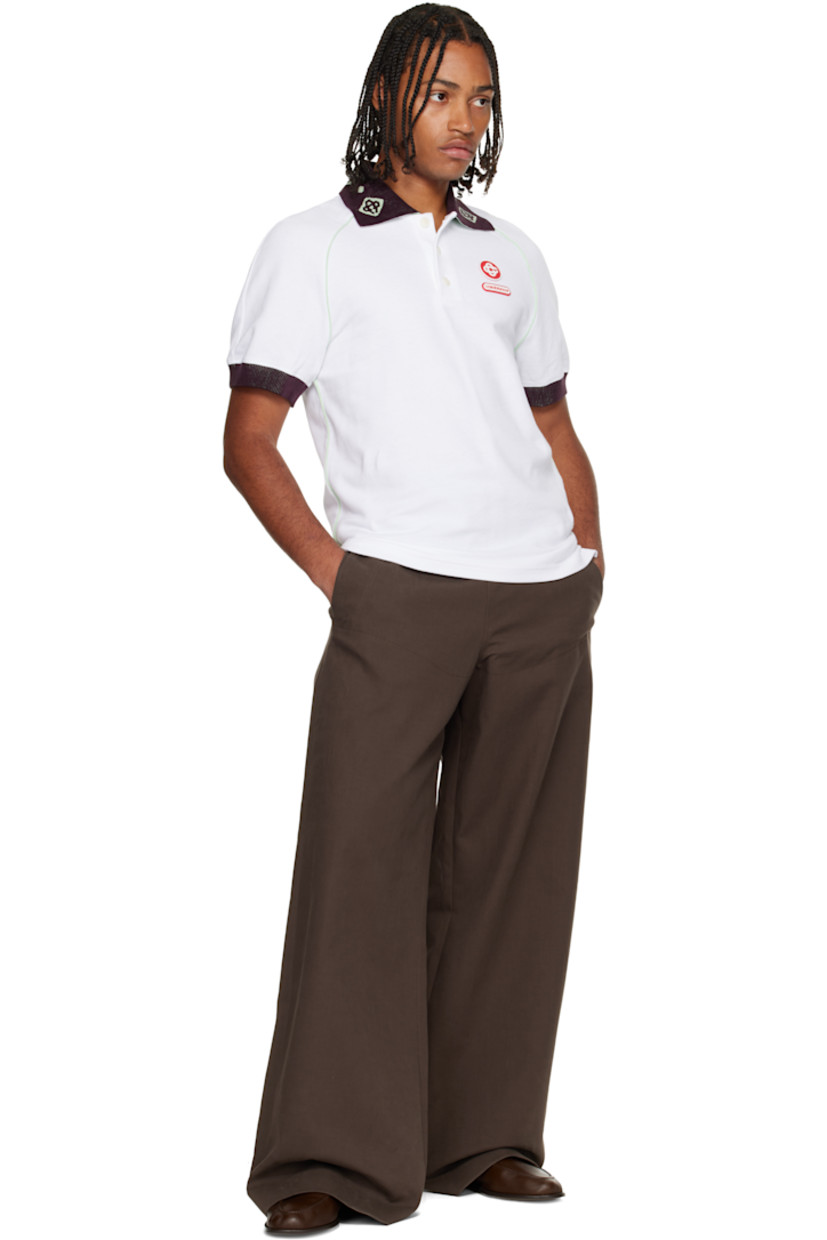 Textured cotton piqué polo.

· Piping throughout 
· Jacquard logo pattern at rib-knit chenille spread collar 
· Three-button placket 
· Rubber logo appliqués at chest and back collar 
· Vented side seams 
· Raglan sleeves 
· Rib-knit chenille cuffs

Supplier color: White