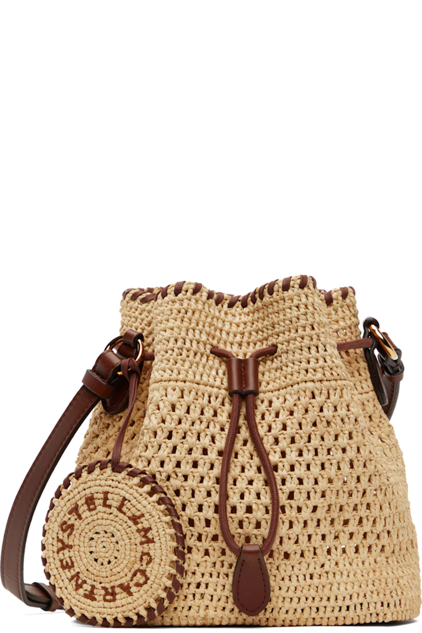 Handcrafted woven raffia tote in beige.

· GOTS-certified organic cotton whipstitching
· Adjustable crossbody strap
· Detachable charm with hand-embroidered logo at strap
· Drawstring closure
· Patch pocket at interior
· H7.5" x W7.5" x D5"

Made from cruelty-free, non-animal materials.

Supplier color: Natural