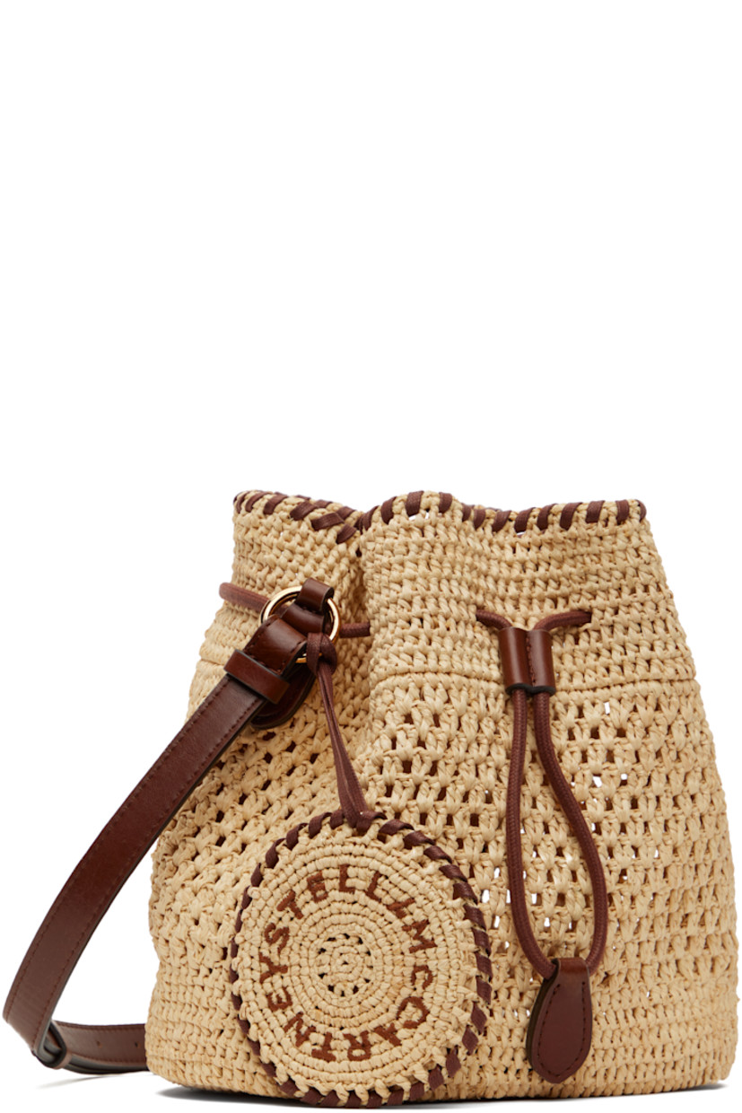 Handcrafted woven raffia tote in beige.

· GOTS-certified organic cotton whipstitching
· Adjustable crossbody strap
· Detachable charm with hand-embroidered logo at strap
· Drawstring closure
· Patch pocket at interior
· H7.5" x W7.5" x D5"

Made from cruelty-free, non-animal materials.

Supplier color: Natural