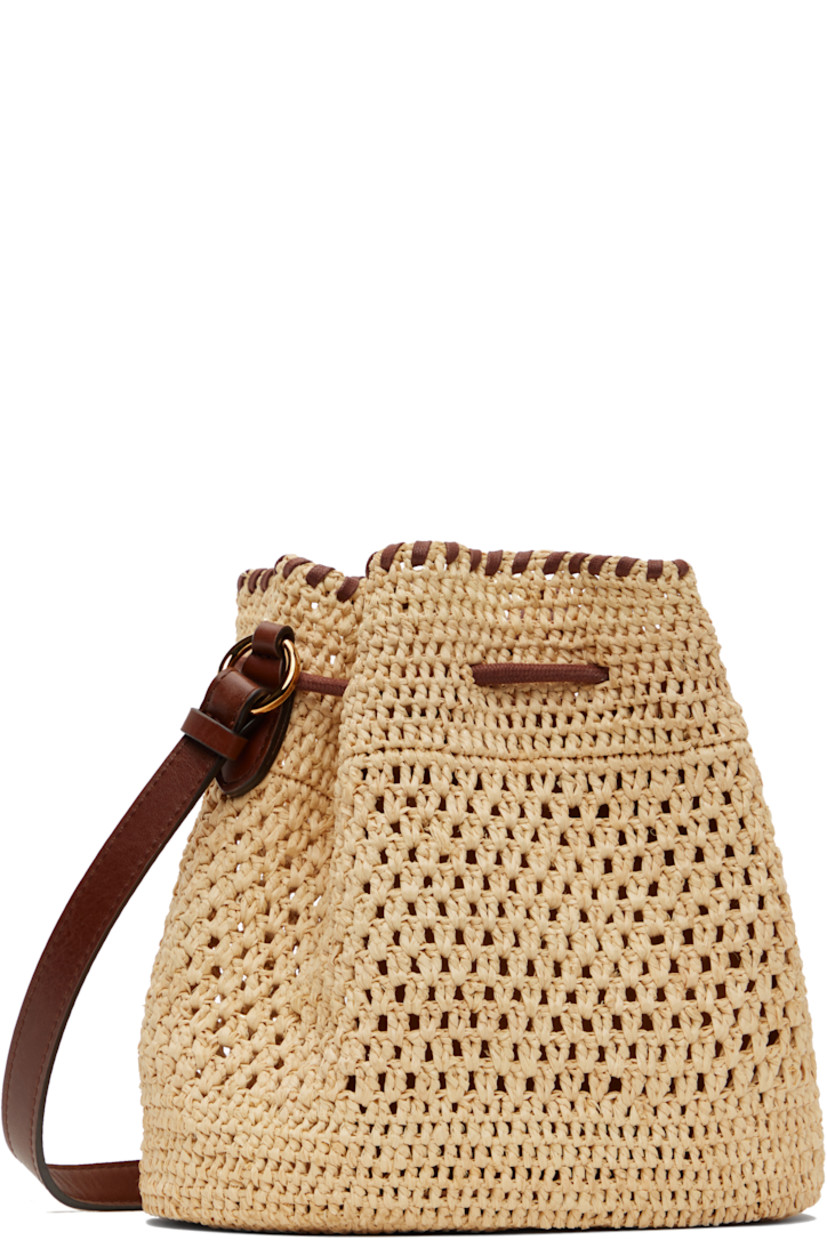 Handcrafted woven raffia tote in beige.

· GOTS-certified organic cotton whipstitching
· Adjustable crossbody strap
· Detachable charm with hand-embroidered logo at strap
· Drawstring closure
· Patch pocket at interior
· H7.5" x W7.5" x D5"

Made from cruelty-free, non-animal materials.

Supplier color: Natural