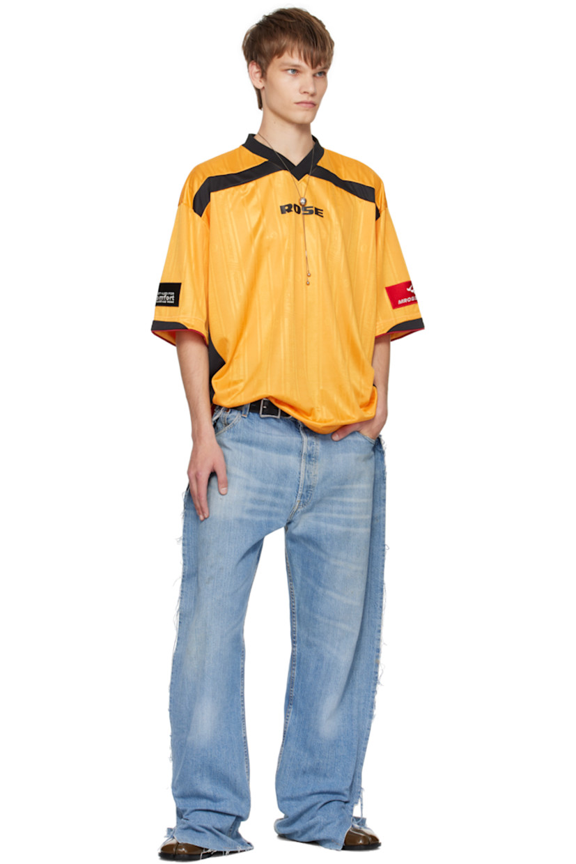 Jersey T-shirt.

· Jacquard graphic pattern throughout
· Rib-knit V-neck
· Logo printed at chest and back
· Piping at hem and cuffs
· Logo patch at cuff
· Text flocked at back

Supplier color: Yellow gold