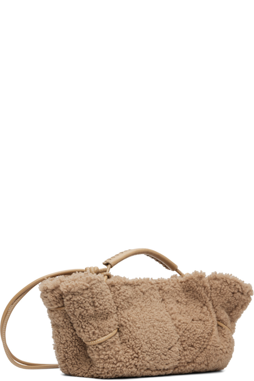 Shearling top handle bag. 

· Whipstitching at rolled carry handle
· Knotted adjustable crossbody strap
· Magnetic closure
· Lambskin lining
· H5.5" x W12" x D4"

Supplier color: Sand