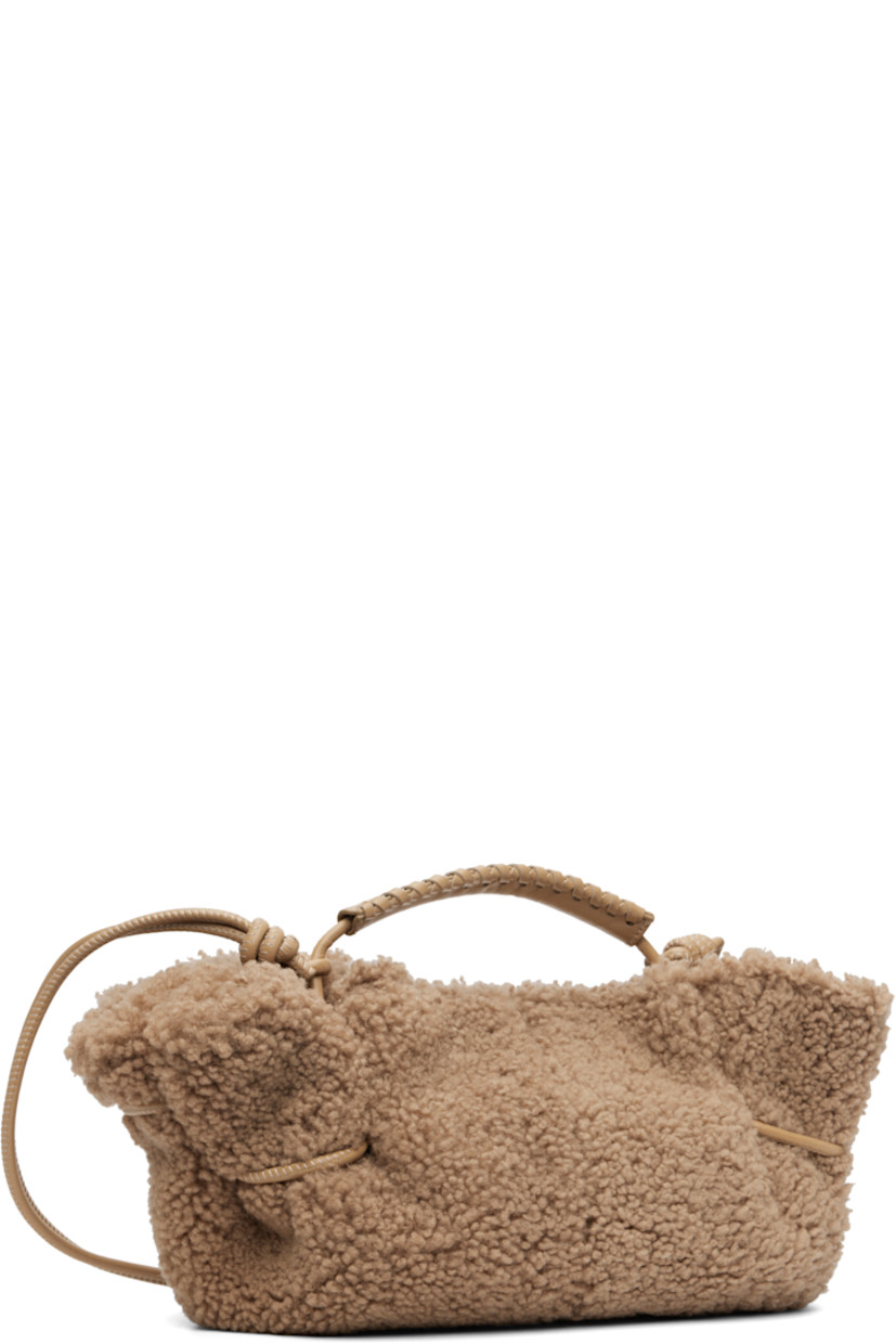 Shearling top handle bag. 

· Whipstitching at rolled carry handle
· Knotted adjustable crossbody strap
· Magnetic closure
· Lambskin lining
· H5.5" x W12" x D4"

Supplier color: Sand
