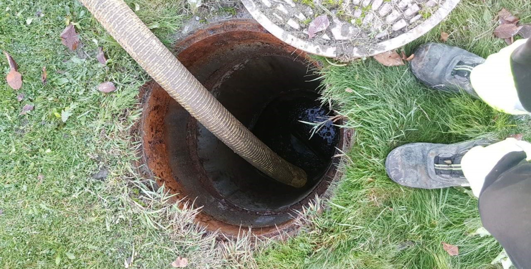 Bilde av en septiktank under tømming og føttene til slamtømmer ved siden av