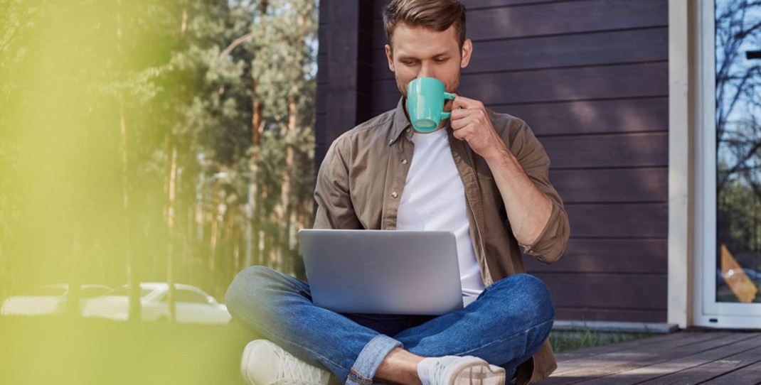 Mann som drikker kaffe og jobber på en laptop