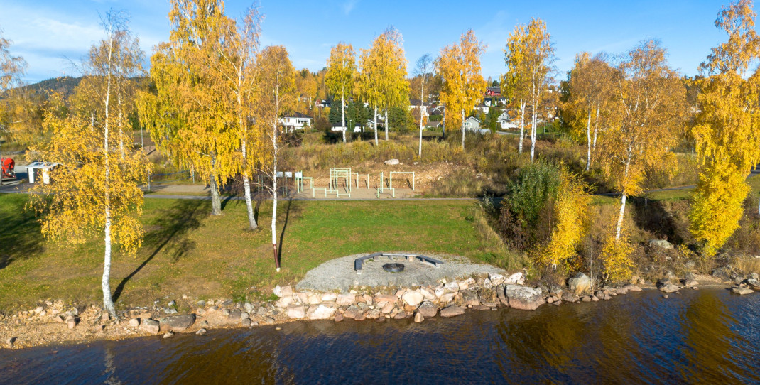 oversiktsbilde av maieriodden tatt fra vannet. Bålplass i forgrunnen og tuftepark lengre bak