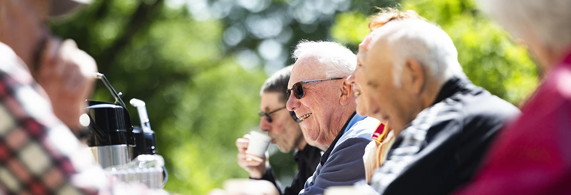 Eldre mennesker som sitter sammen rundt et bord ute i skogen