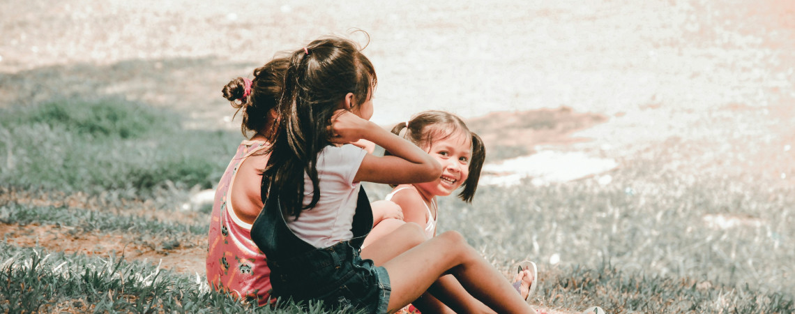 Fotografi av tre barn som sitter i gresset. To av barna ser mot høyre i bildet, det tredje barnet ser mot fotografen.