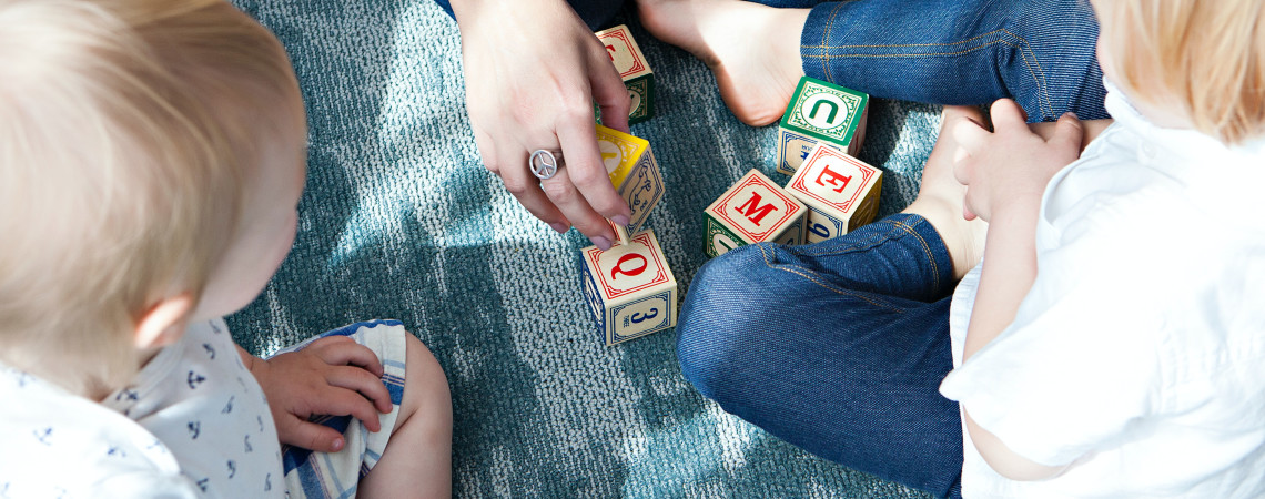 voksenhender og barneføtter på et gulv med lekeklosser