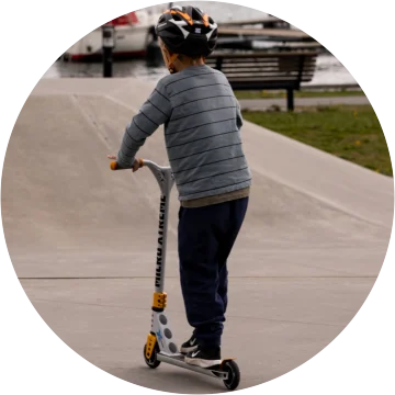 Barn som står på sparkesykkel i skatepark.