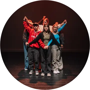 Seks barn står på en scene, tett sammen og holder hender i en slags stjerneformasjon.