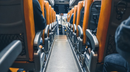 gang mellom seter i en moderne buss, sett bakfra med passasjerer sittende på begge sider.