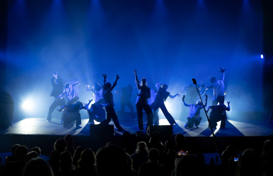 Mange dansere på en scene. Kraftige skygger i blått lys.