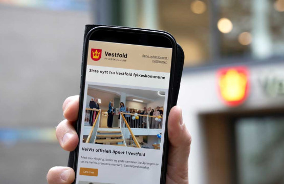 En hånd holder en mobiltelefon som viser et nyhetsbrev fra Vestfold fylkeskommune