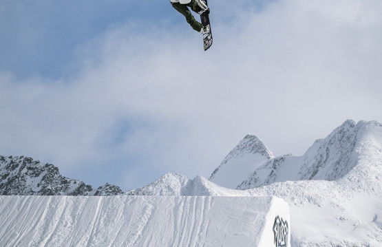 Snowboarder som hopper høyt opp fra et hopp i Alpene.