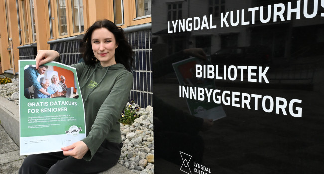 Bilde av Tora Helene Johnsen på utsiden av biblioteket med plakaten som informerer om gratiskurset DIGI hjelp