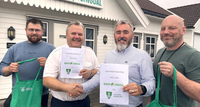 Bilde av fire personer foran bygget til Radio Lyngdal, de holder opp den signerte samarbeidsavtalen som er inngått mellom radioen og Lyngdal kommune
