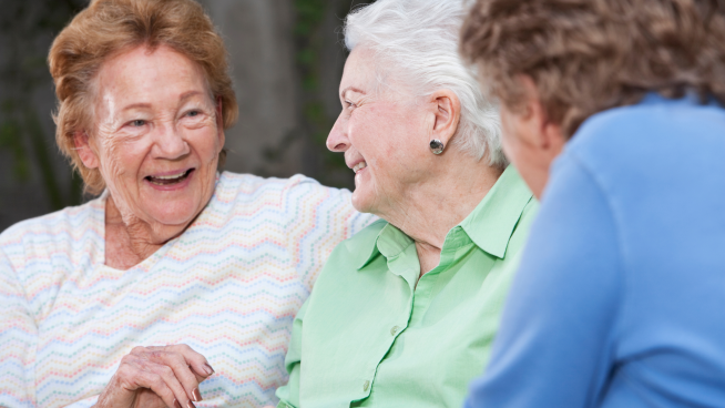 Tre smilende seniordamer i samtale.