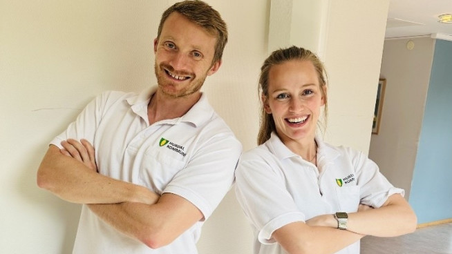 To fysioterapeuter, en mann og en kvinne, som smiler og står lent mot hverandre