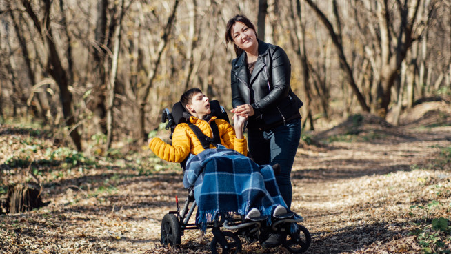 En gutt som sitter i rullestol og en kvinne som er ute og går tur.