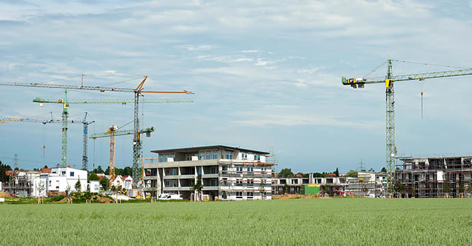 Eine Baustelle eines neuen Wohngebietes mit mehreren Baukränen. Einige Mehrfamilienhäuser sind noch eingerüstet.