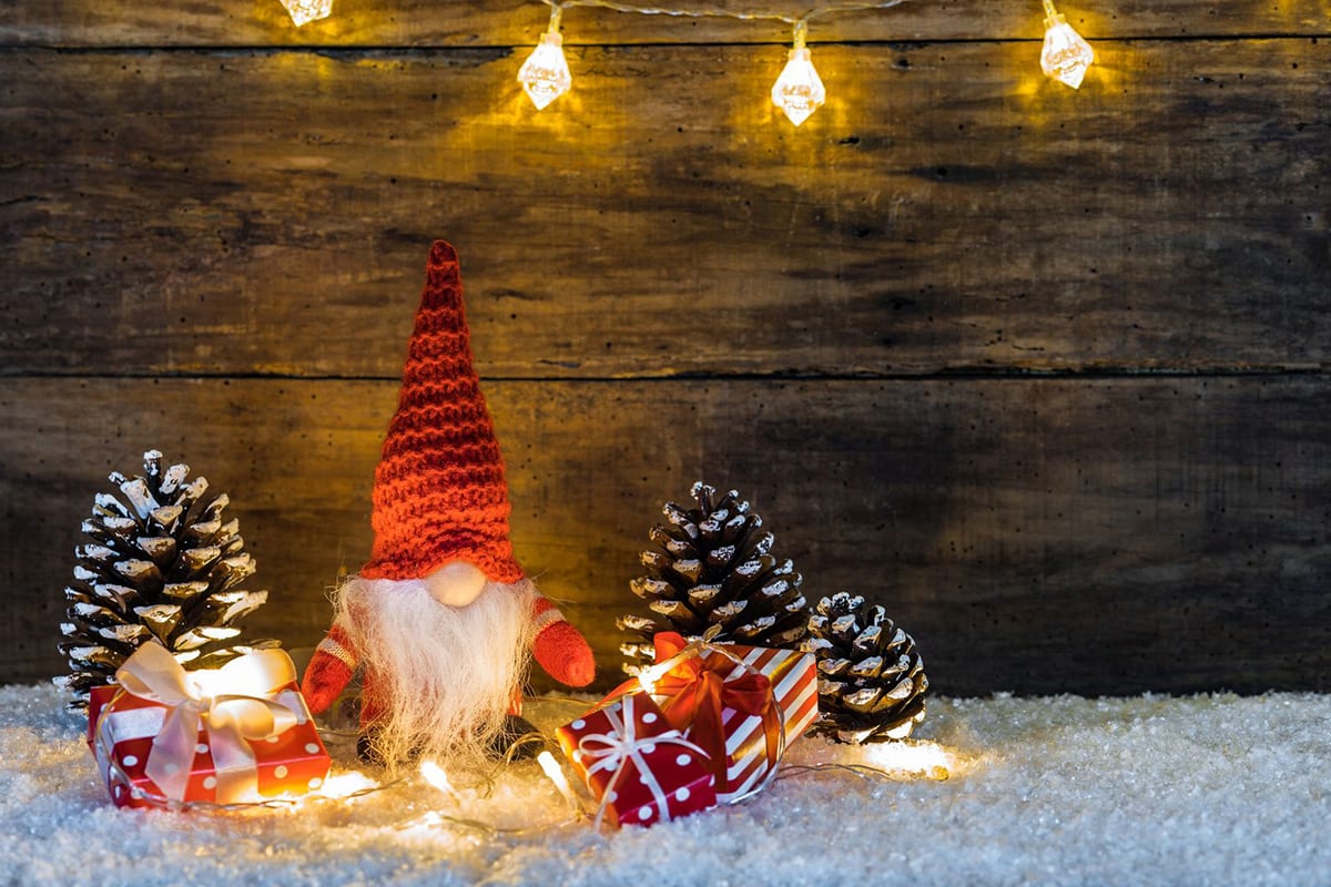 Weihnachtsgruß der Stadtwerke Sindelfingen Eine kleine Wichtelfigur steht zwischen Tannenzapfen und einer Lichterkette auf einer weißen, schneebedeckten Oberfläche.