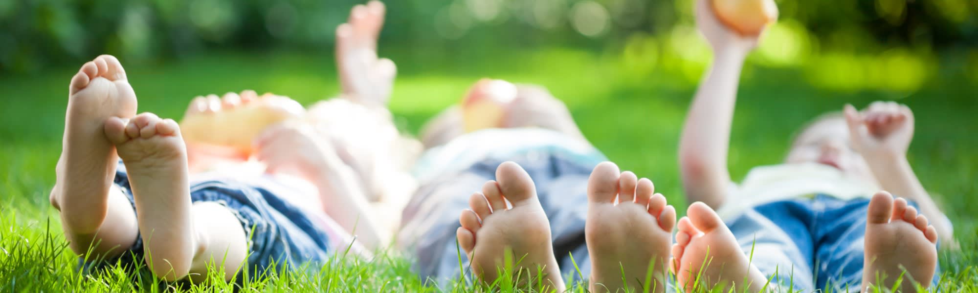Drei Kinder liegen auf dem Gras, die Füße in Richtung des Betrachters. Körper und Gesicht sind unscharf.