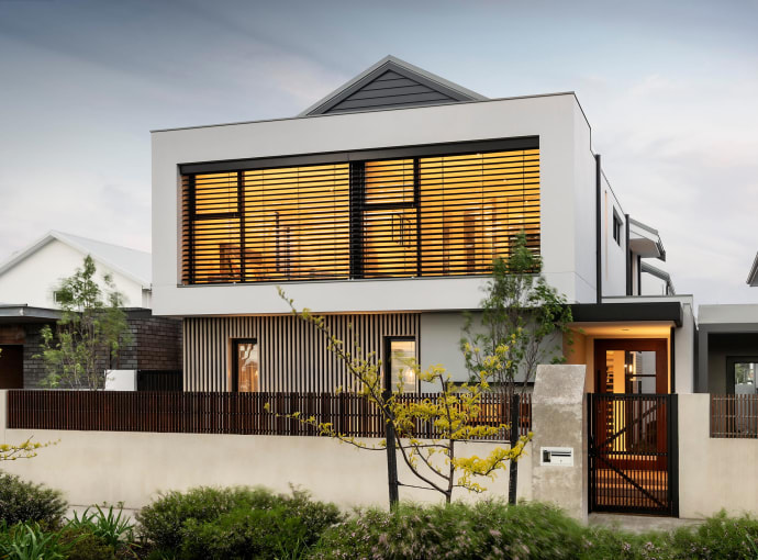 Exterior of a modern two-story luxury home in Perth at dusk, featuring warm interior lighting and vertical timber slats.