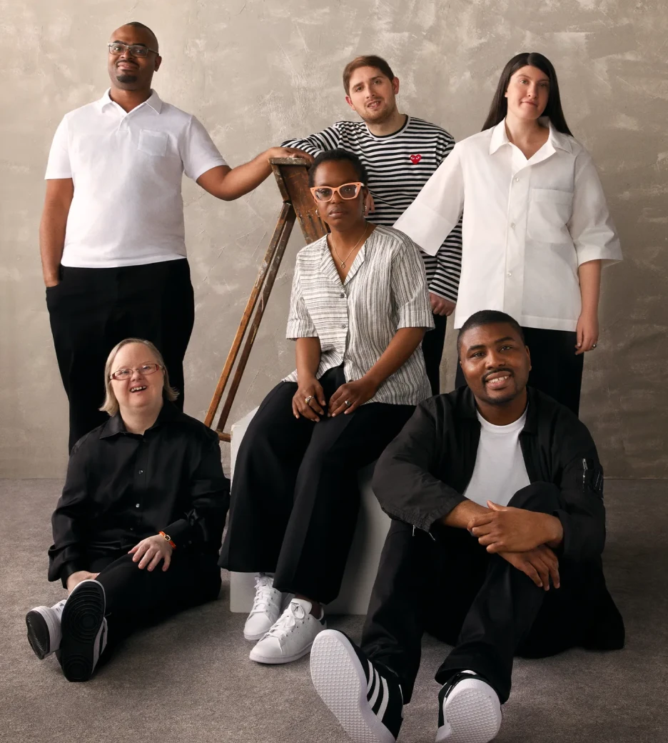 Six people in standing and seated positions, all wearing a variation of white and black clothing.