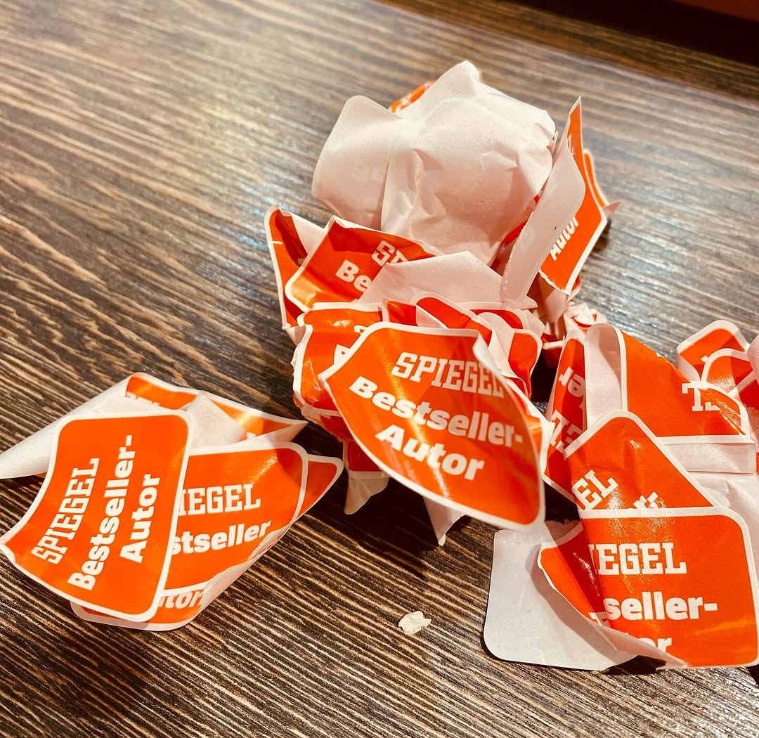 Nahaufnahme einer Tischplatte mit vielen abgeknibbelten, aufeinander geworfenen Stickern, auf denen SPIGEL-Bestseller-Autor steht.