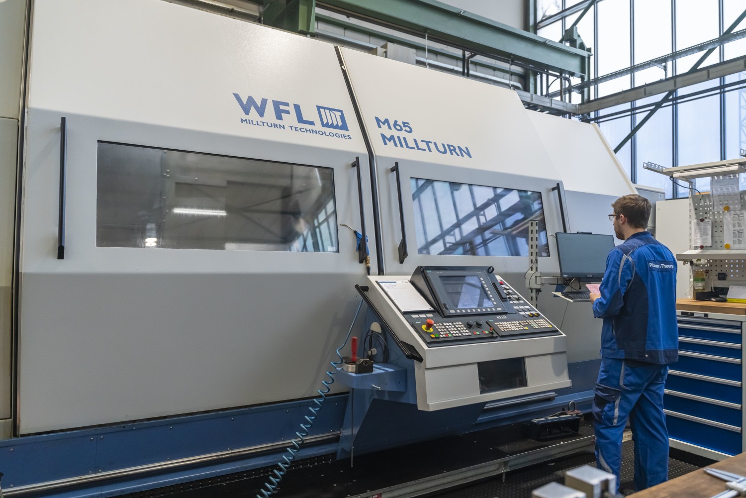 Blick auf die generalüberholte Gebrauchtmaschine Millturn M65 von WFL; am Bedienpult steht ein Mitarbeiter von Plasser & Theurer