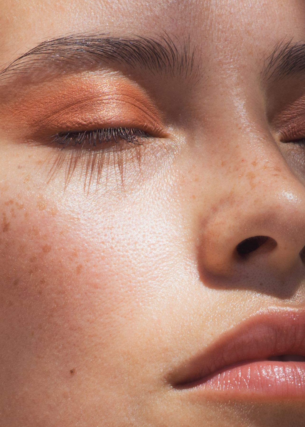 Close-up of a young woman wearing orange eye shadow.