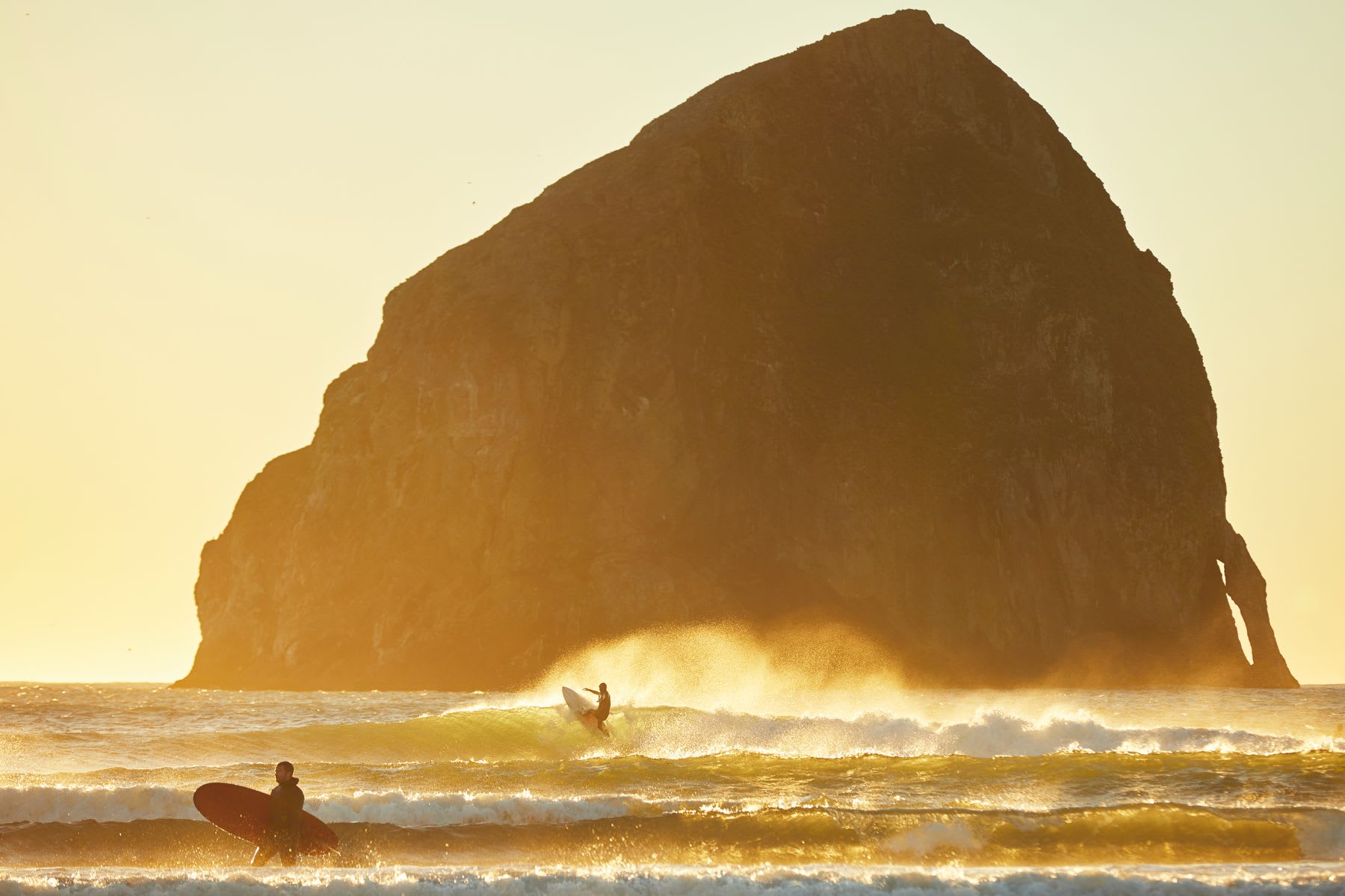 Person surfs a wave in front of Haystack rock at Cape Kiwanda in pacific city, oregon.