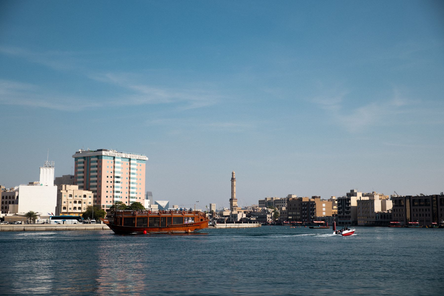 A cityscape with buildings, a wooden boat and a speedboat under a blue sky