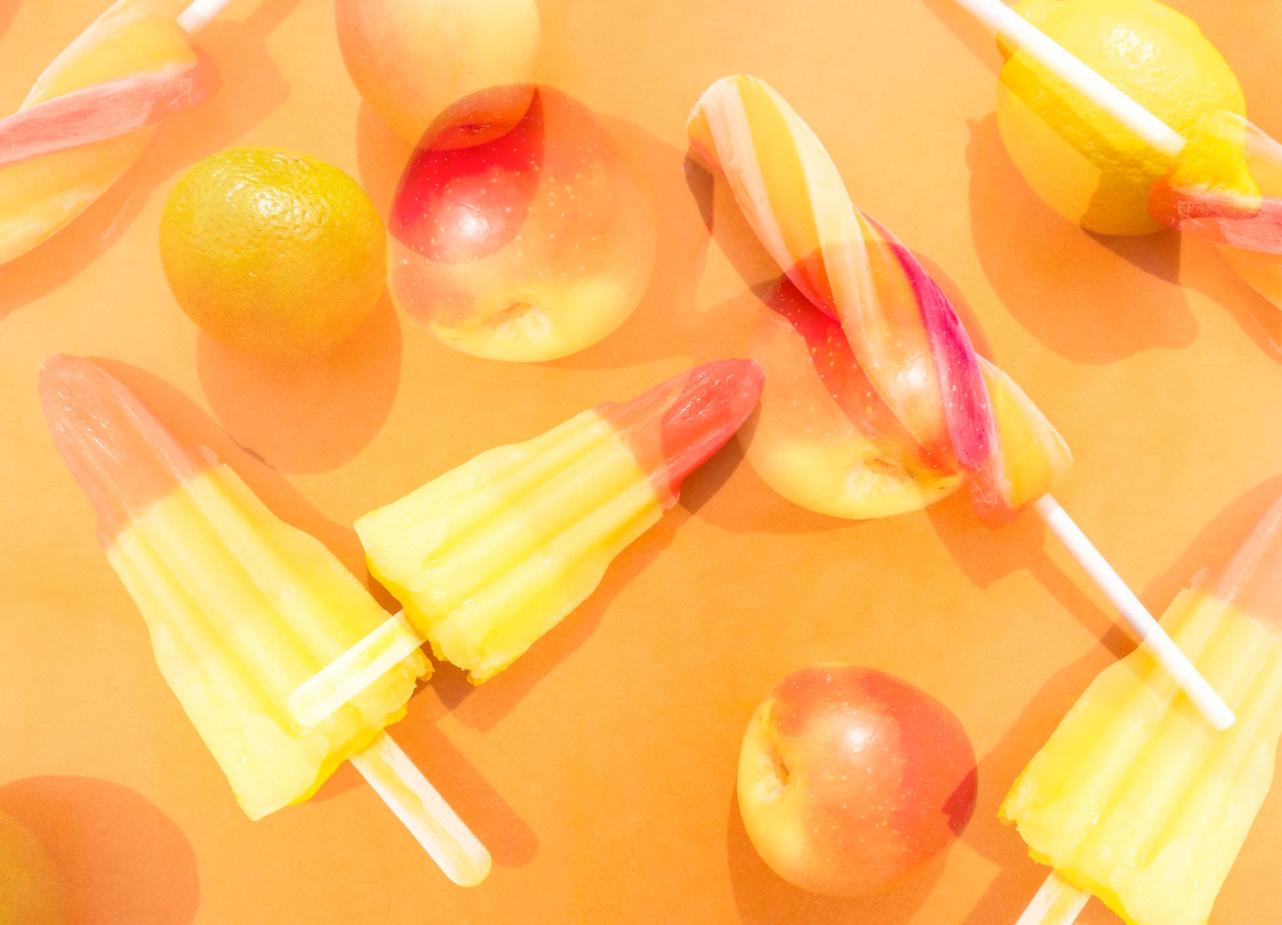 Popsicles and spiral popsicles on an orange background with apples and lemons