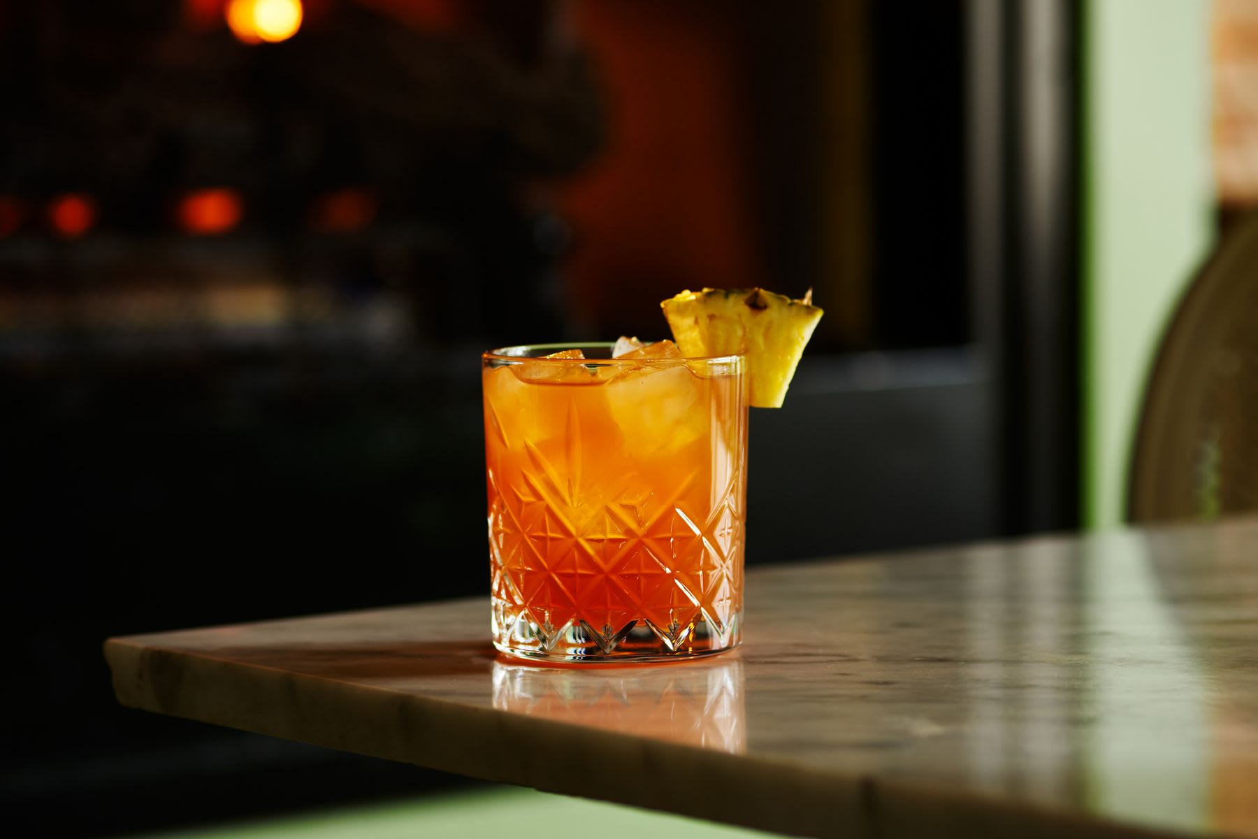 An orange-colored cocktail with a slice of lemon garnish on a marble table.